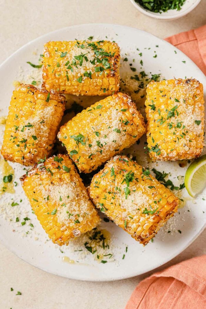 An overhead shot shows the air fried frozen corn cobs served on a white plate with garnishes on top