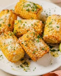 A close shot shows frozen corn cobs air fried to golden juicy delicious served on a white plate with sprinkles on top