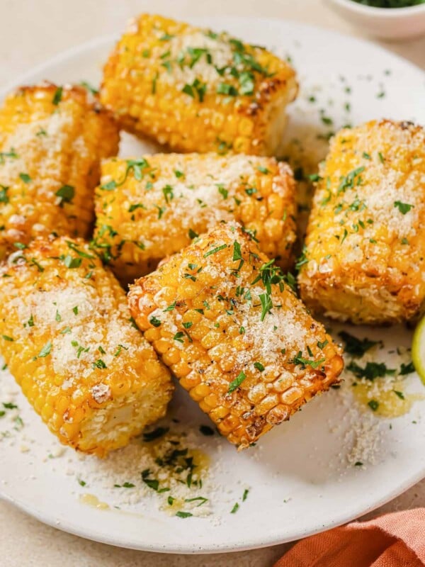 A close shot shows frozen corn cobs air fried to golden juicy delicious served on a white plate with sprinkles on top