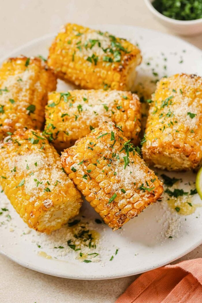 A close shot shows frozen corn cobs air fried to golden juicy delicious served on a white plate with sprinkles on top