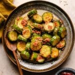 A recipe image for Korean spicy cucumber salad with a wooden fork on the side of the plate.