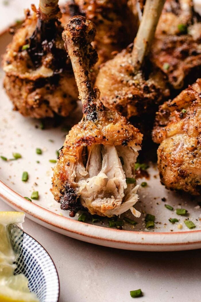 A close side shot shows a chicken lollipop after one bite with juicy meat exposed on a serving plate