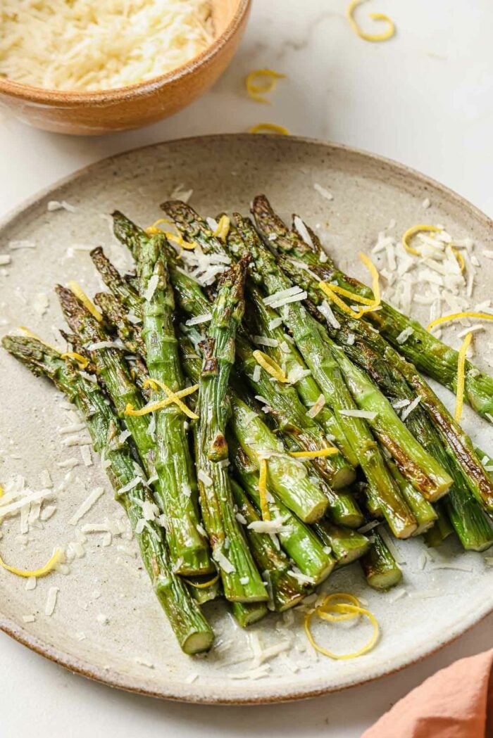 A side close shot shows air fryer frozen asparagus spears cooked and served on a neutral color plate with garnishes on the side