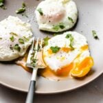 A side close shot shows 3 air fryer poached eggs served on a light gray color plate with a fork