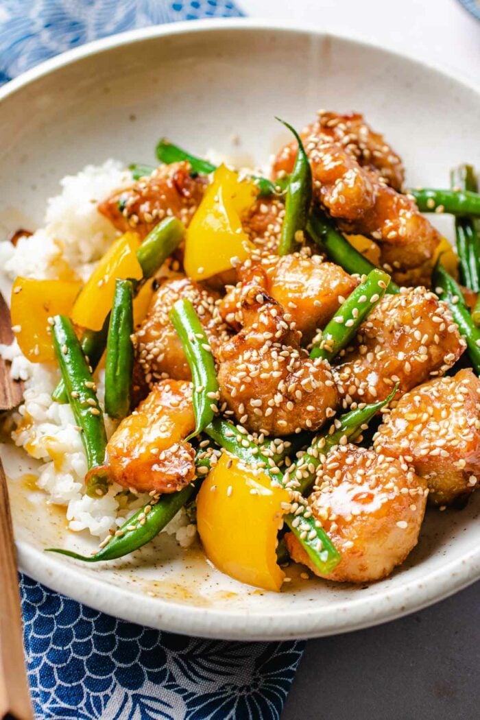 A side close shot of panda honey sesame chicken served in a white plate with rice on the side