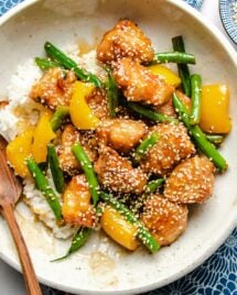 A close overhead shot shows golden brown chicken breasts with green beans and yellow bell pepper honey sesame sauce served over a white plate.