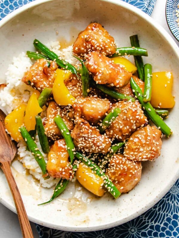 A close overhead shot shows golden brown chicken breasts with green beans and yellow bell pepper honey sesame sauce served over a white plate.