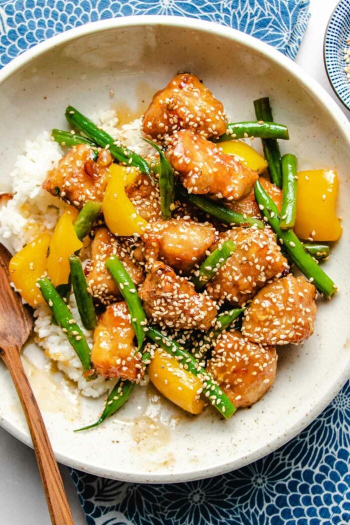 A close overhead shot shows golden brown chicken breasts with green beans and yellow bell pepper honey sesame sauce served over a white plate.