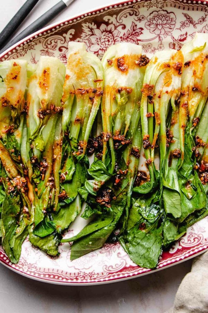 An overhead shot shows a big plate of roasted bok choy served on a platter with garlic chili sauce