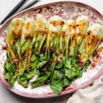 Roasted bok choy recipe served on a big white/red plate with chili garlic sauce