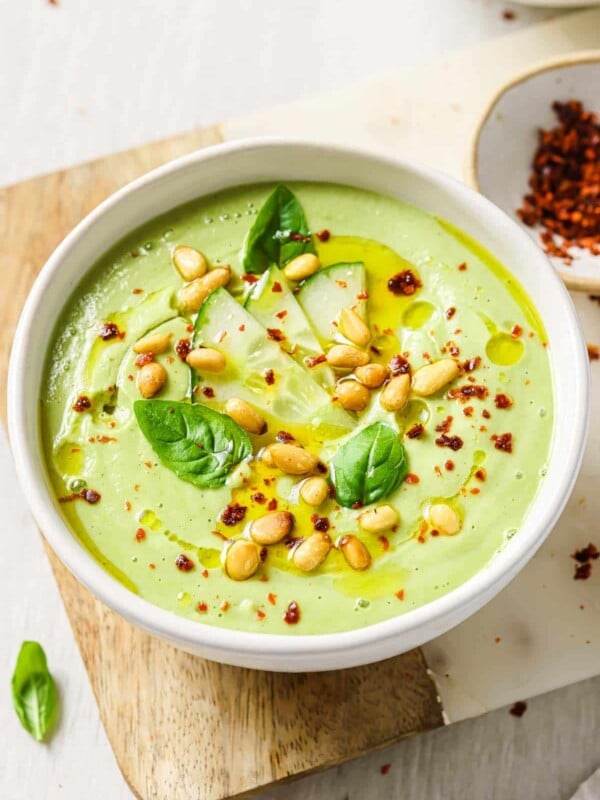 An image shows cucumber gazpacho served in a white bowl with chili pepper flakes on the side.