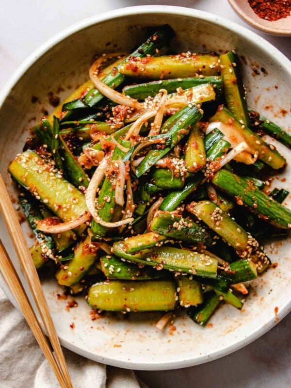 An overhead close shot shows cucumber kimchi served in a white plate with chopsticks on the side.