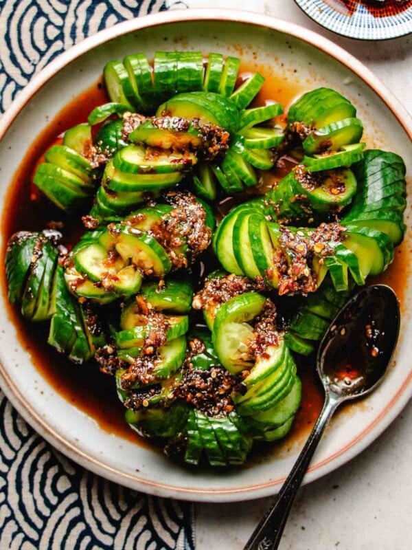 Photo shows the dish Spicy Cucumber Salad spiral-cut served with Chinese chili dressing on a light colored plate with chili sauce on the side.