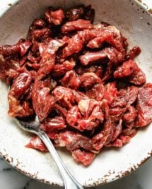 A close shot shows thinly sliced beef marinated with tenderize seasoning in a white bowl