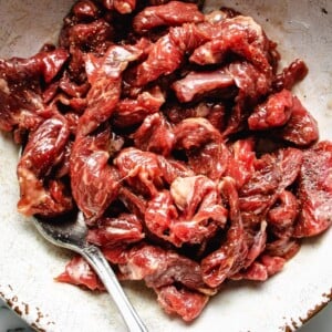 A close shot shows thinly sliced beef marinated with tenderize seasoning in a white bowl