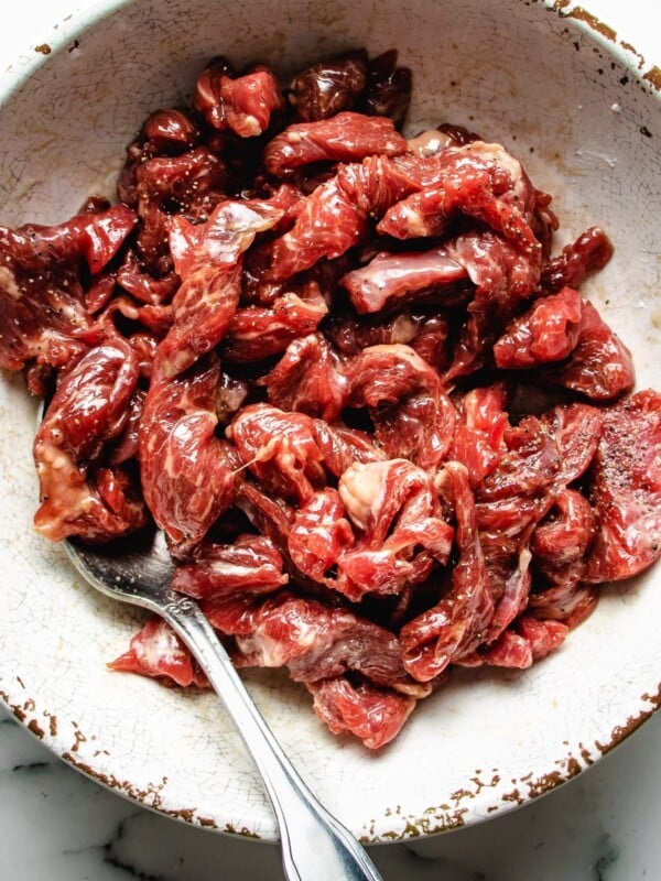 A close shot shows thinly sliced beef marinated with tenderize seasoning in a white bowl