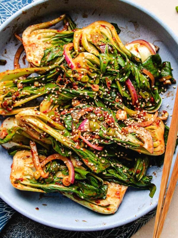 A close shot photo shows bok choy marinated with kimchi sauce and served in a blue plate.