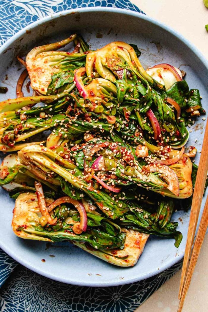 A close shot photo shows bok choy marinated with kimchi sauce and served in a blue plate.