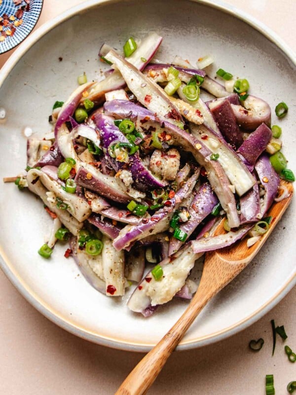 A close shot shows steamed Chinese eggplants shredded with garlic and soy seasonings on top served in a white plate