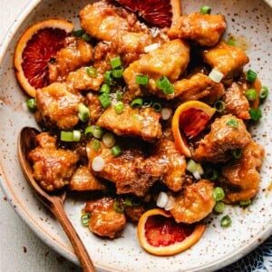 Photo shows homemade Panda express orange chicken served in a white plate with fresh slices of oranges.