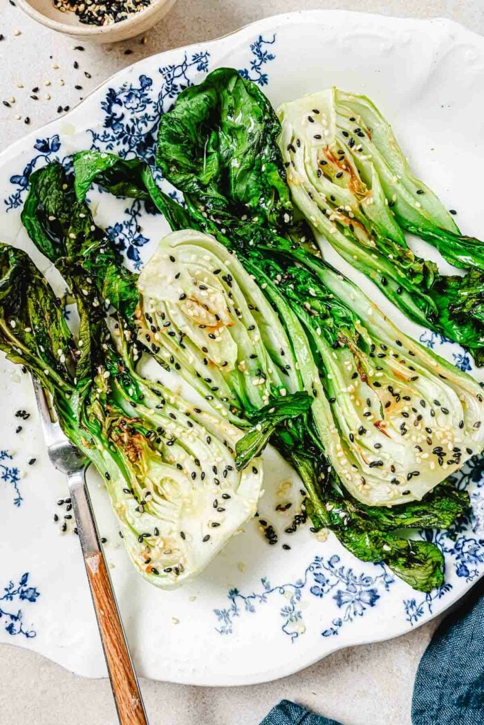 A close shot photo shows baby bok choy air fried and served on a blue white color plate