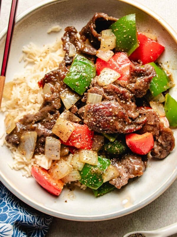 Photo shows black peppercorn beef stir fried with bell peppers and served with rice on a white plate