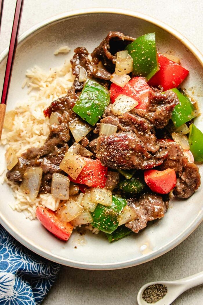 Photo shows black peppercorn beef stir fried with bell peppers and served with rice on a white plate