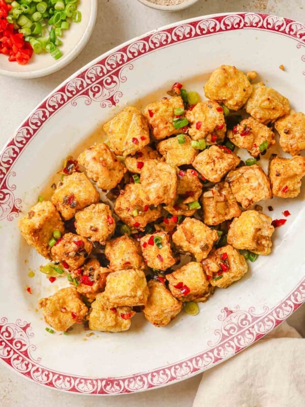 Photo shows air fryer salt and pepper tofu served on a white plate with salt pepper seasoning on the side.