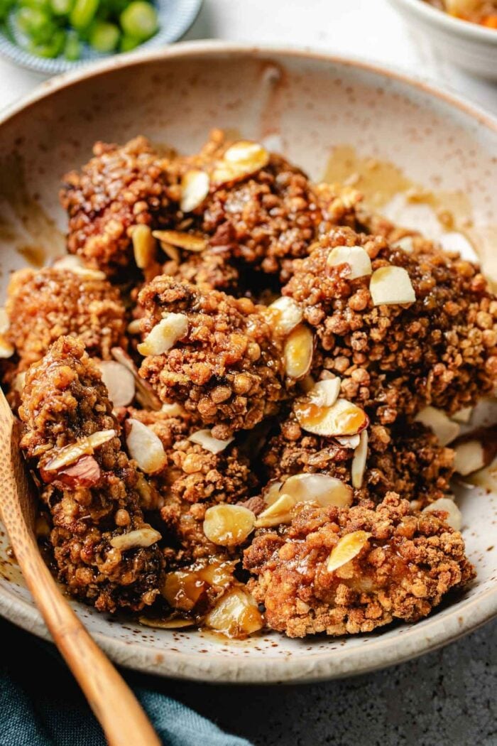 A side close shot photo shows puff rice breaded crunchy almond chicken breast chunks with almond slices and sauce served in a white plate