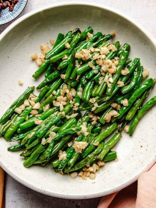 Image shows Din tai fung copycat green beans with crisp exterior and topped with loads of minced garlic served in a white plate.