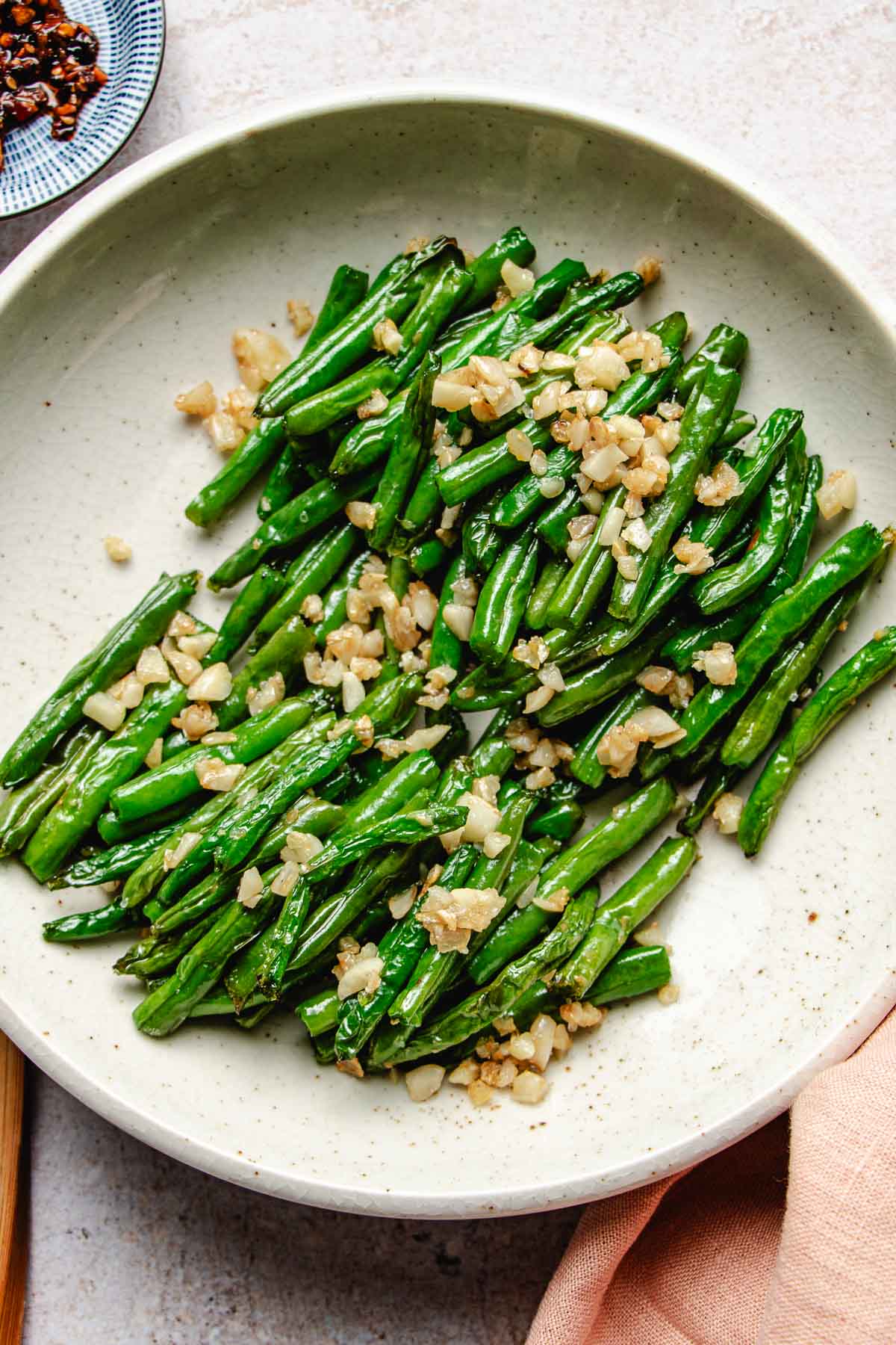 Image shows Din tai fung copycat green beans with crisp exterior and topped with loads of minced garlic served in a white plate.