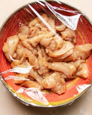 Image shows chicken breast thinly sliced and seasoned with baking soda to tenderize the meat before stir frying
