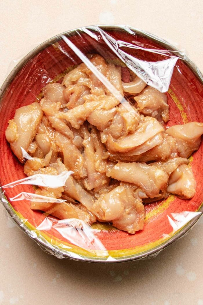 Image shows chicken breast thinly sliced and seasoned with baking soda to tenderize the meat before stir frying