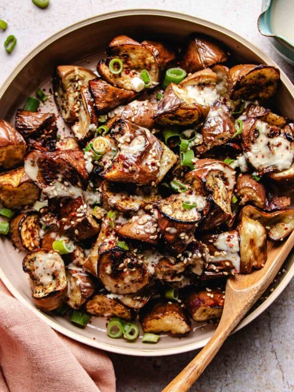 Image shows Roasted cubed Chinese eggplant served in a big round plate drizzled with a creamy sauce on top