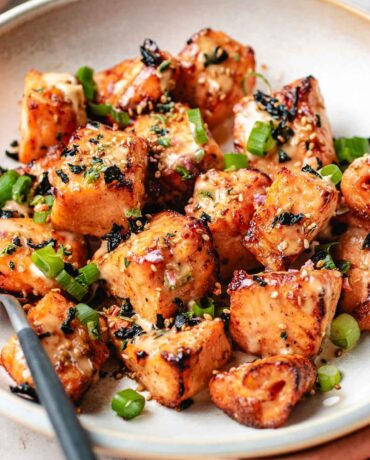 Salmon chunks sliced and seasoned then either air fried or oven baked and coated with bang bang sauce on a plate.
