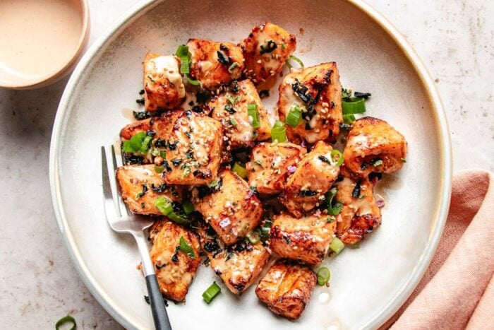 A feature image shows salmon bites drizzled with bang bang sauce and served in a white plate.