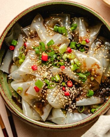 Photo shows a plate of rice paper noodles made with rice paper sheets with garnishes and sauce on top