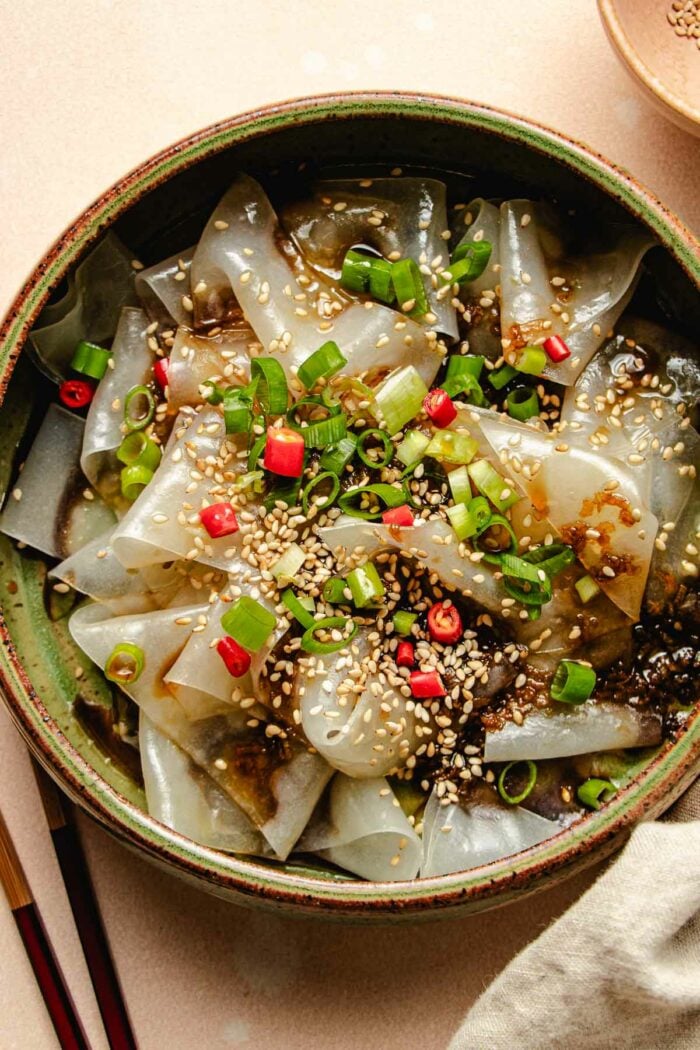 Photo shows a plate of rice paper noodles made with rice paper sheets with garnishes and sauce on top