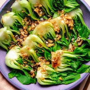 A purple plate filled with steamed baby bok choy with garlic and oyster sauce drizzled on top.