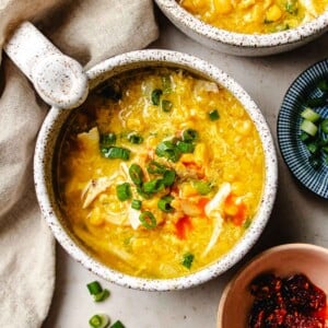 Chicken corn egg drop soup recipe image shows a bowl of soup served in a white mug with chili sauce drizzled on top.