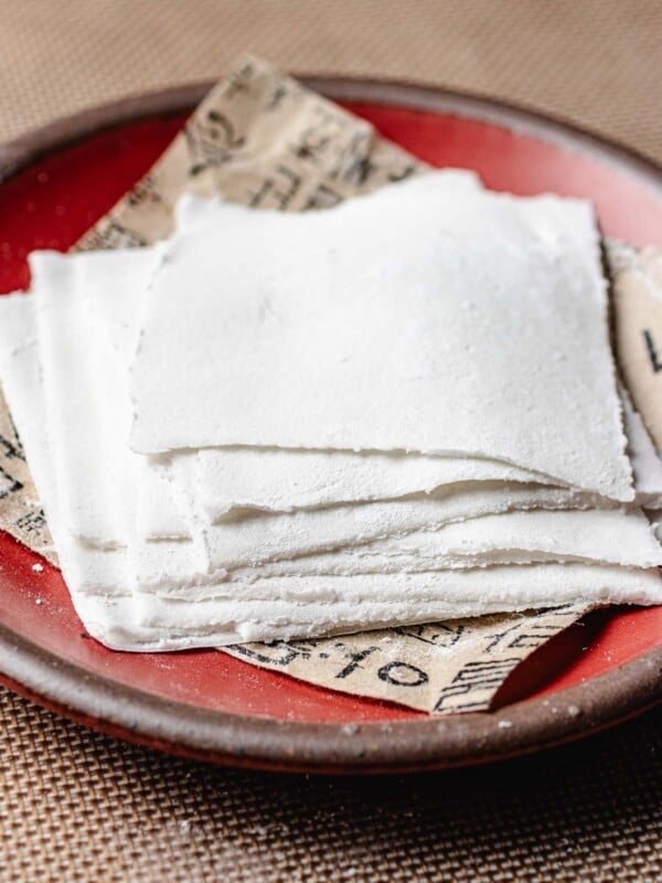 Feature image shows homemade gluten free wonton wrappers that are thin square pieces stacked on a red color plate.