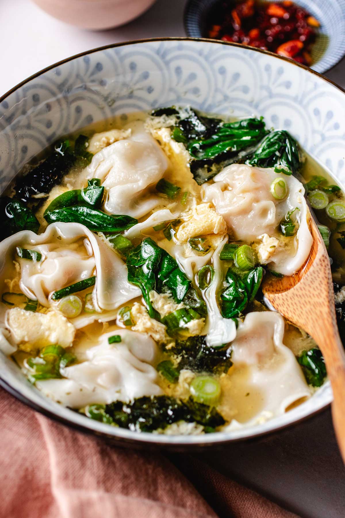 A side close shot image shows soft wontons floating in fluffy egg flower broth with spinach and seaweed in the broth.