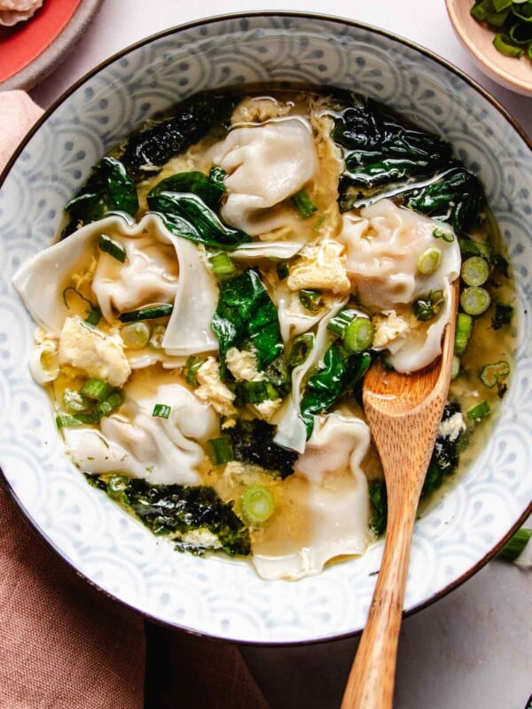 Feature image shows silky soft wontons boiled and served in a bowl of egg drop soup with spinach and seaweed in the bowl.