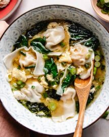 Feature image shows silky soft wontons boiled and served in a bowl of egg drop soup with spinach and seaweed in the bowl.