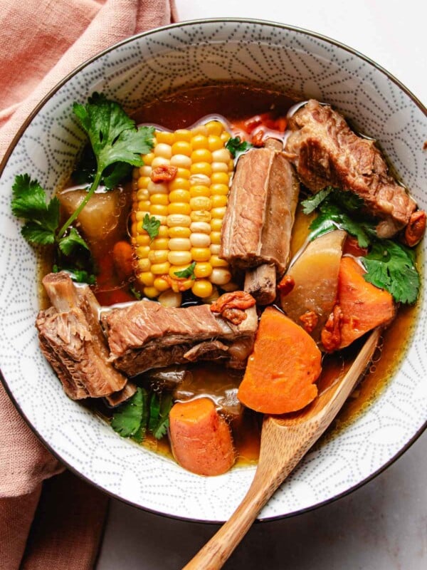 Feature image shows tender pork ribs soup simmered with daikon radish, carrots, and corn and served in a white soup bowl.