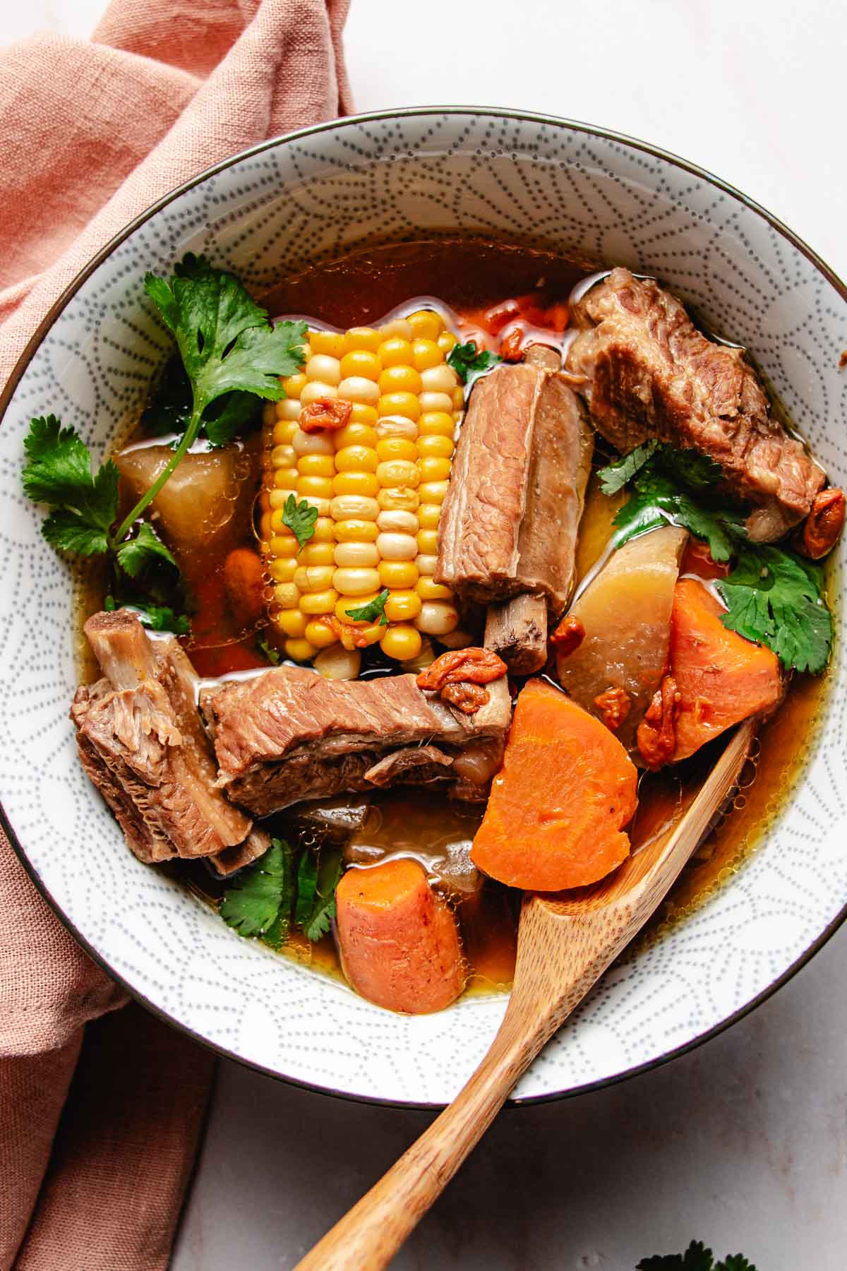 Feature image shows tender pork ribs soup simmered with daikon radish, carrots, and corn and served in a white soup bowl.