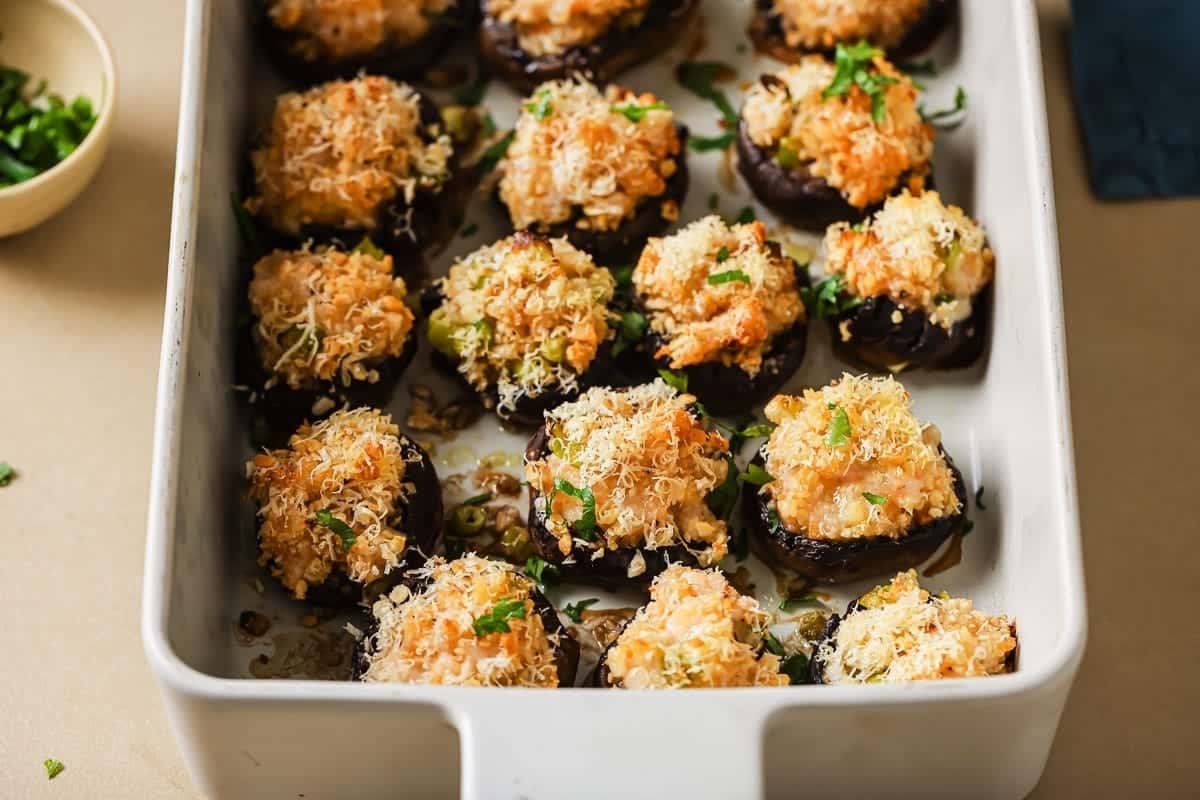 A baking dish filled with shrimp stuffed mushrooms, topped with a golden, crispy cheese and breadcrumb mixture, and garnished with chopped parsley.