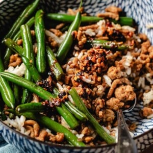 Feature image shows ground chicken and green beans stir fried and served in a blue color bowl with steamed rice.