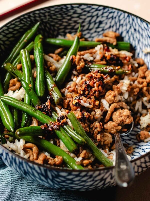 Feature image shows ground chicken and green beans stir fried and served in a blue color bowl with steamed rice.