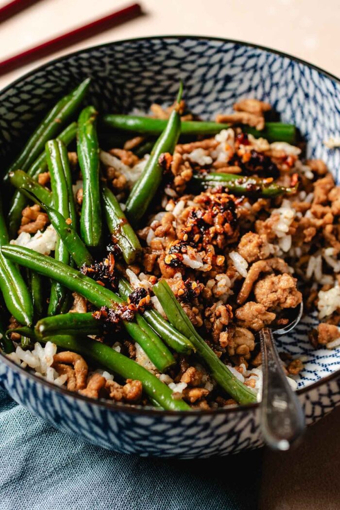 Feature image shows ground chicken and green beans stir fried and served in a blue color bowl with steamed rice.